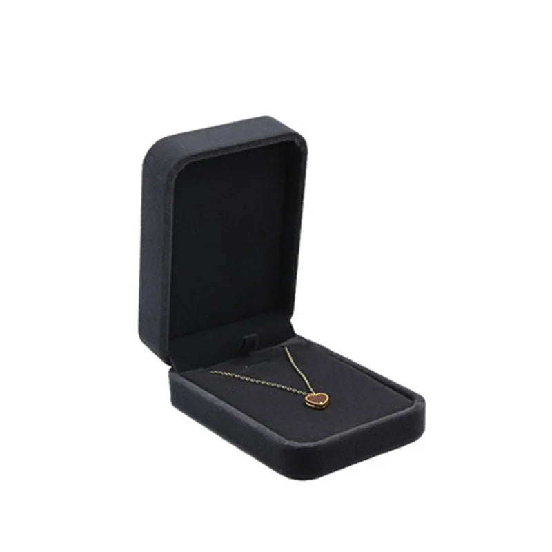 An open black velvet jewelry box displaying a delicate gold necklace with a small oval pendant on a plain white background.