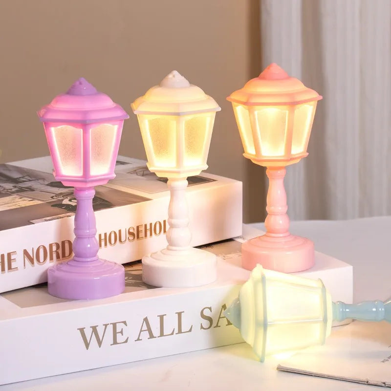 Three colorful lamp-shaped night lights on a surface with books in the background.