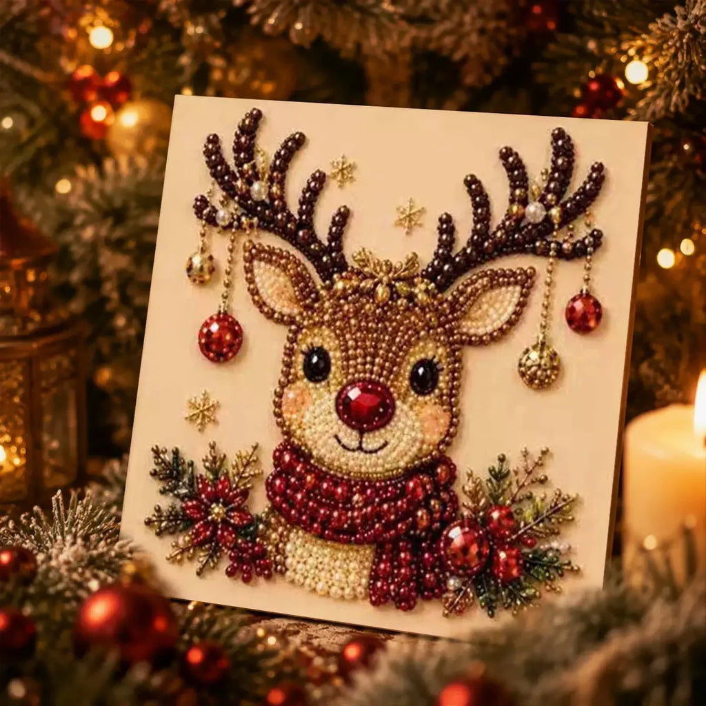 A square beaded Christmas art piece featuring a reindeer with large antlers, a red nose, and a red-and-gold beaded scarf, surrounded by holiday ornaments and evergreen branches in a warm festive setting.