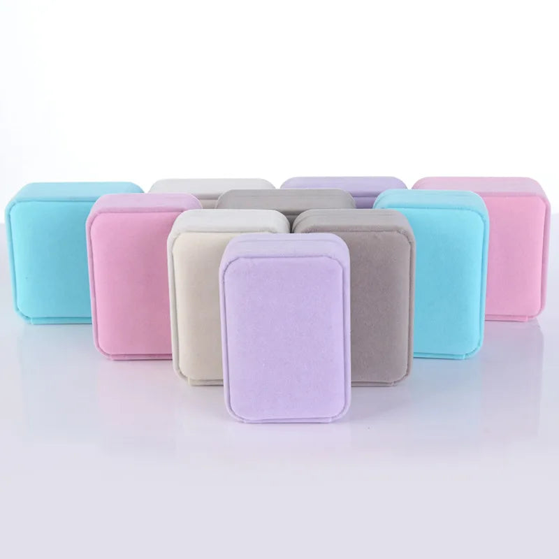 A set of small rectangular fabric pouches or cases in pastel colors, including light blue, pink, cream, lavender, taupe, and purple, arranged in rows on a white reflective surface.