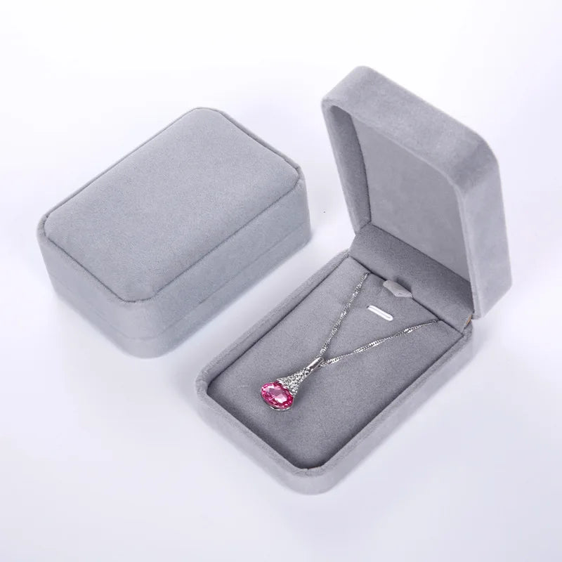Silver necklace with a pink gemstone in an open gray velvet jewelry box on a white background