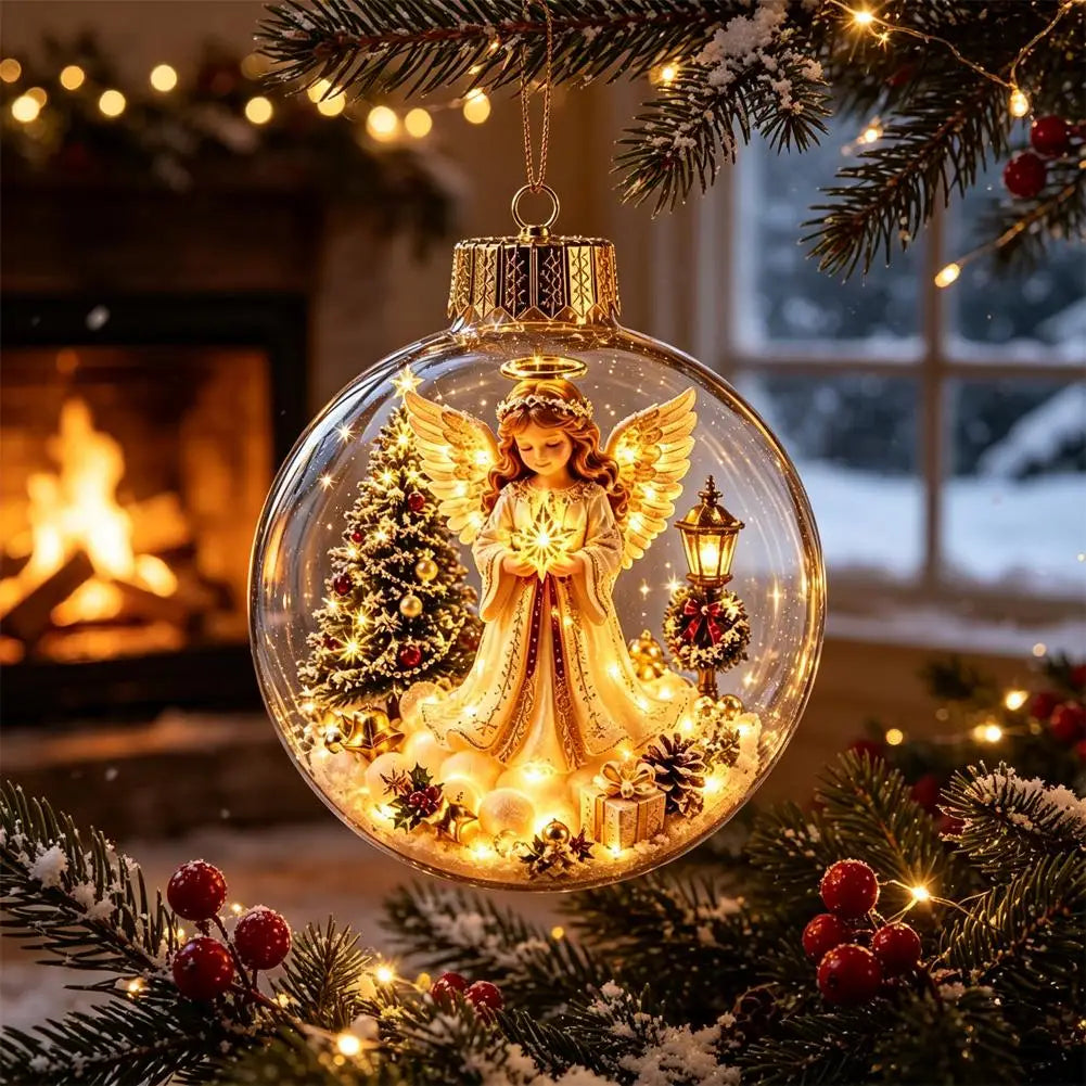 A clear glass Christmas ornament hangs from a pine branch in a cozy holiday setting. Inside the ornament is a golden angel figure with wings, surrounded by a small lit Christmas tree, warm fairy lights, pinecones, and a lantern.