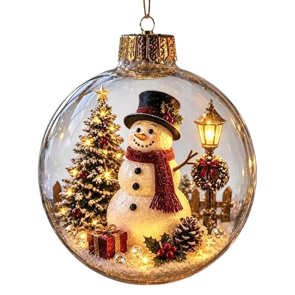 A clear glass Christmas ornament ball hanging from a gold cap, featuring a festive winter scene with a snowman wearing a black hat and red scarf, a lit Christmas tree, gifts, pinecones, holly, and a glowing street lamp inside.