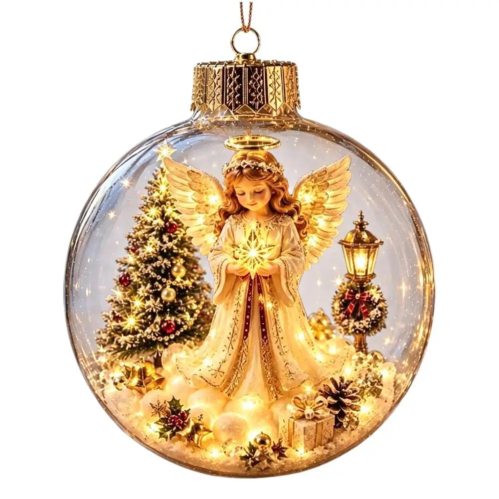 A clear round Christmas ornament with a gold cap and hanging loop, featuring a golden angel figurine in a snowy scene with a lit Christmas tree, gift boxes, pinecones, and a lantern inside.