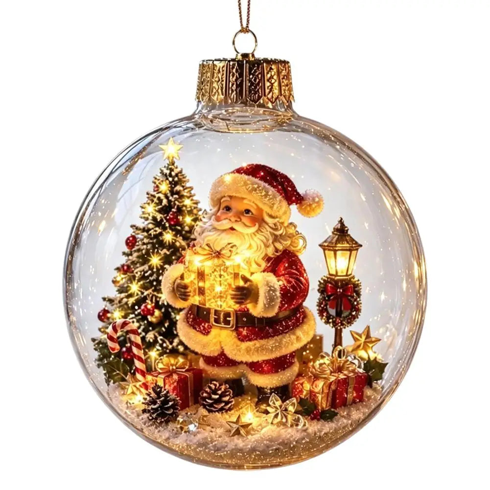A clear glass Christmas ornament ball hanging from a gold cap, featuring a festive Santa Claus scene with a glowing gift box, decorated tree, lantern, and wrapped presents inside.