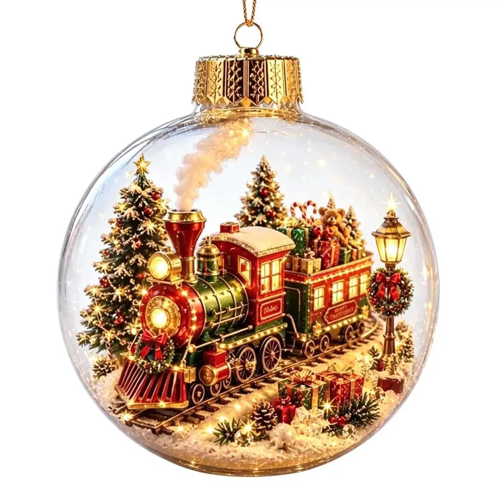 A clear glass Christmas ornament ball featuring a miniature festive scene with a red and green steam train, decorated Christmas trees, warm glowing windows, gift boxes, and a lit streetlamp, hanging from a gold cap on a white background.