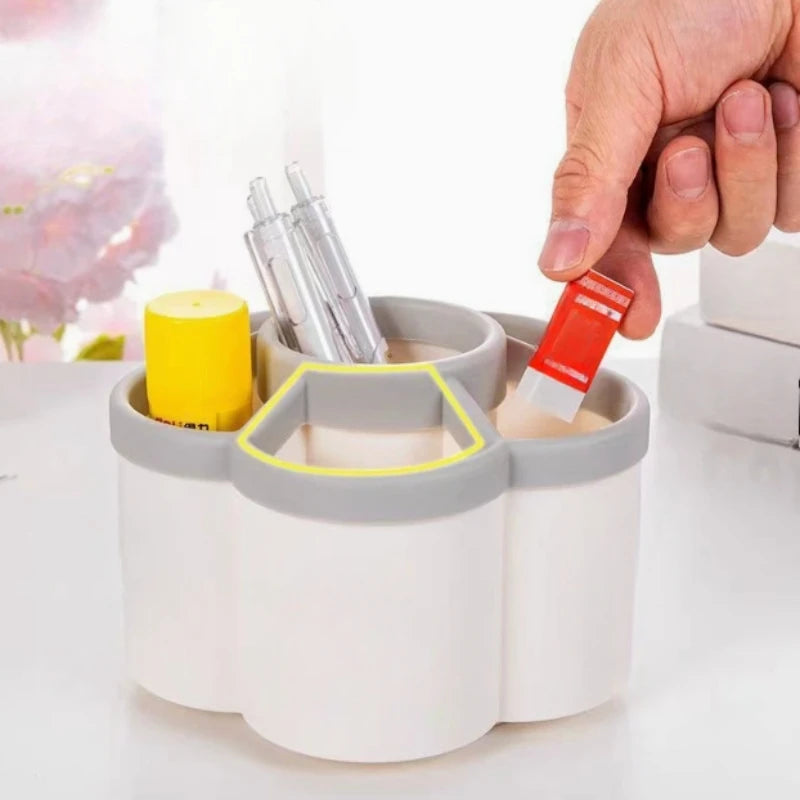  Hand placing a red eraser into one of the six compartments of a white rotating desk organizer with yellow and silver pens on a bright white surface