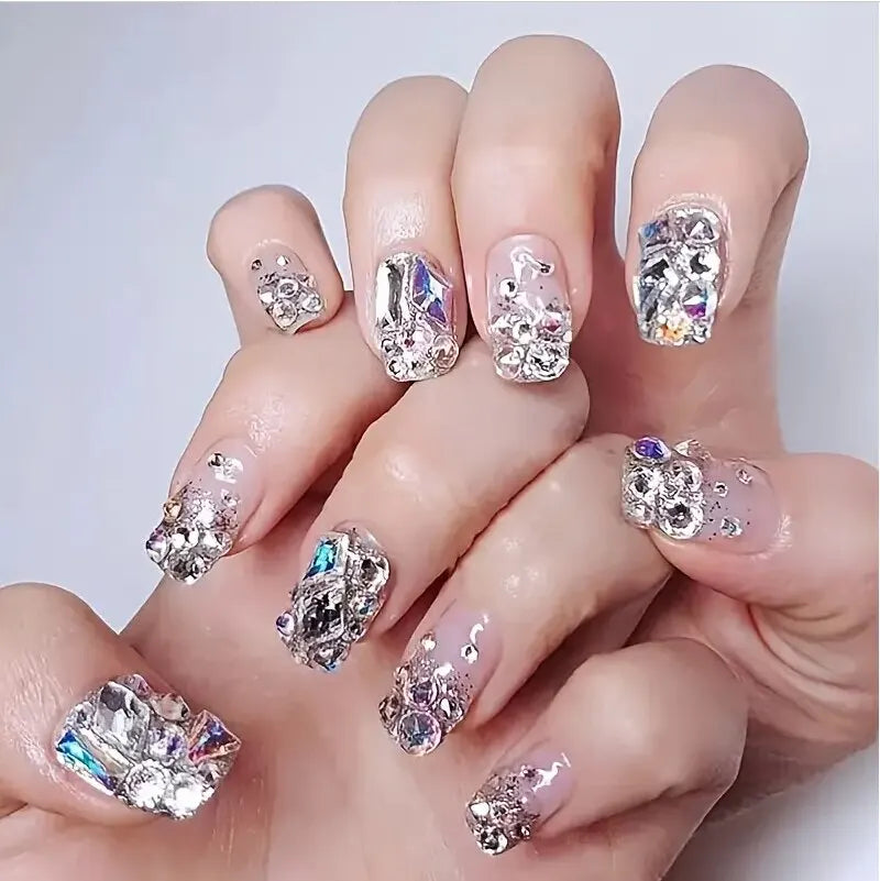 Hand with ornate nail art featuring crystals and gemstones on a light background